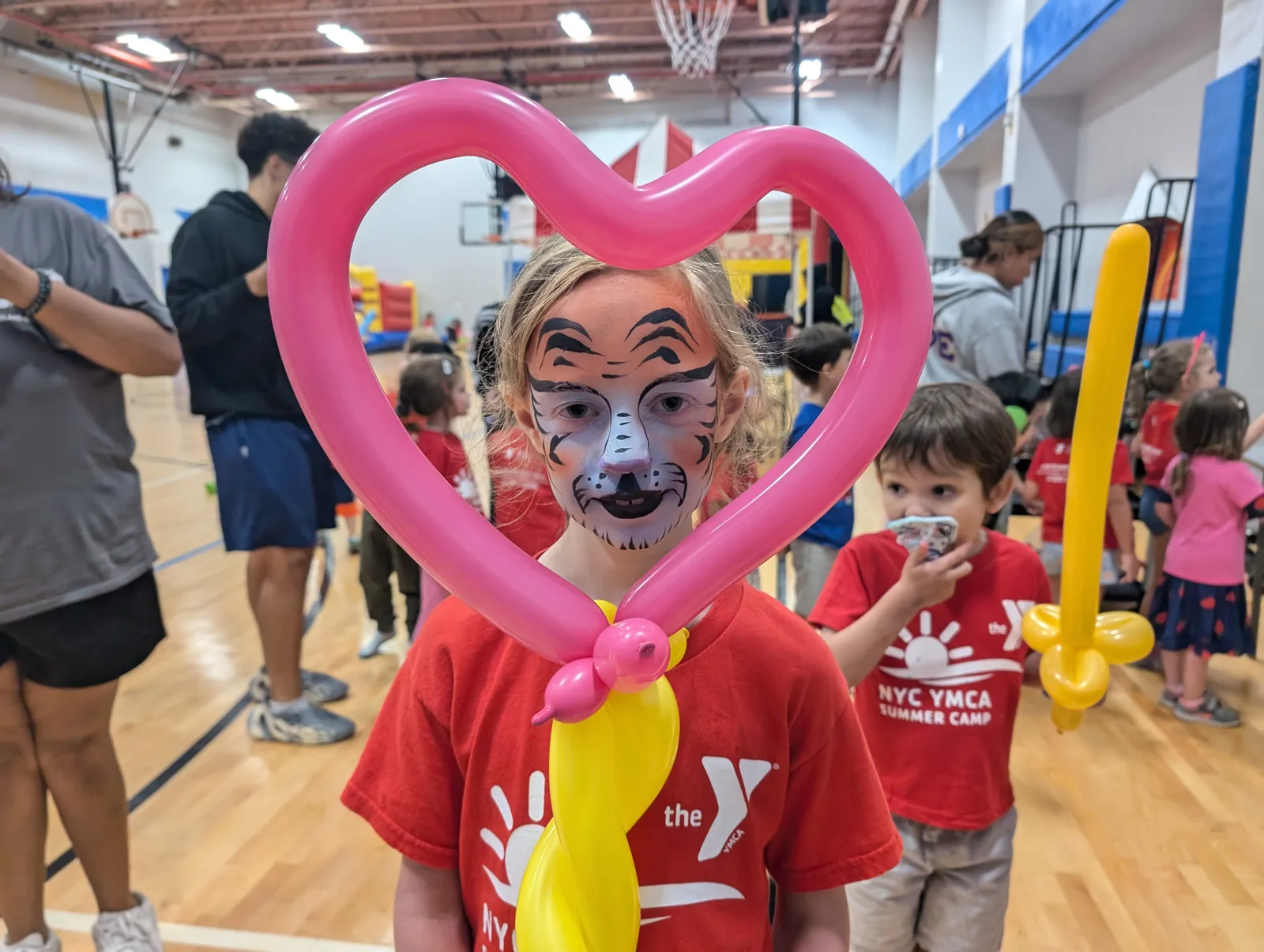 A child with tiger face paint holding a pink heart-shaped balloon