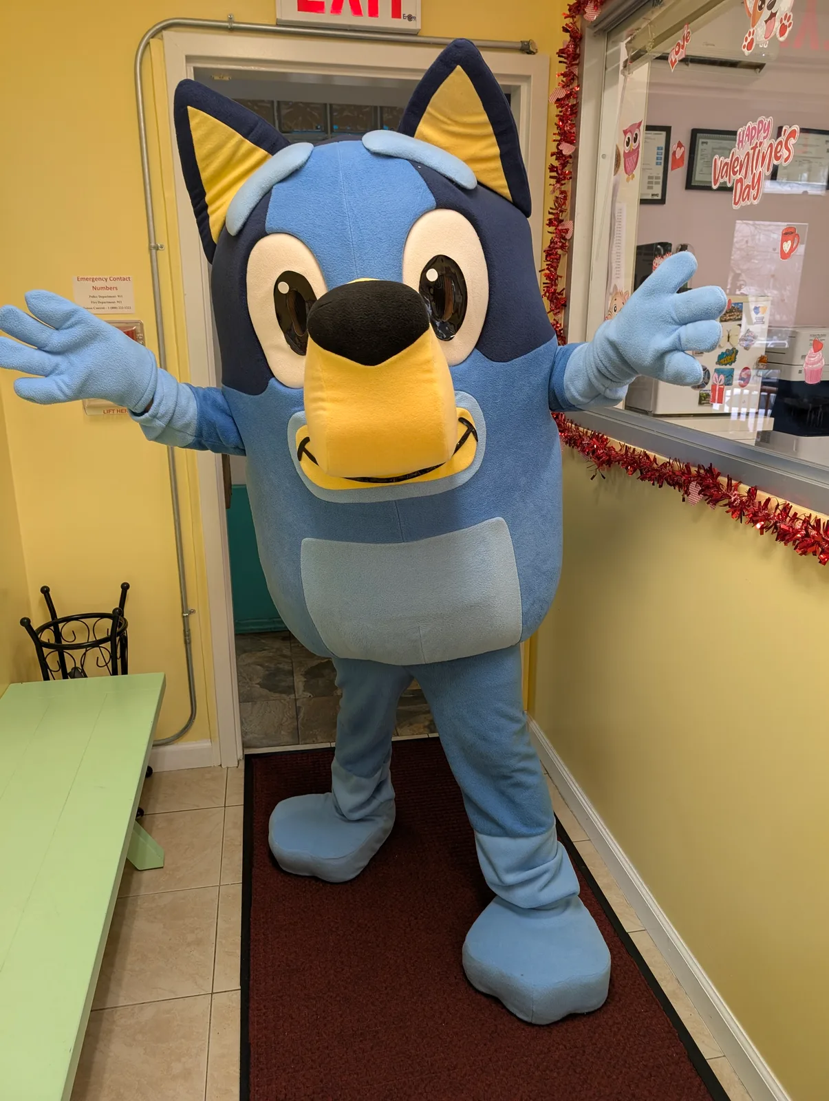A blue dog mascot waving inside a home