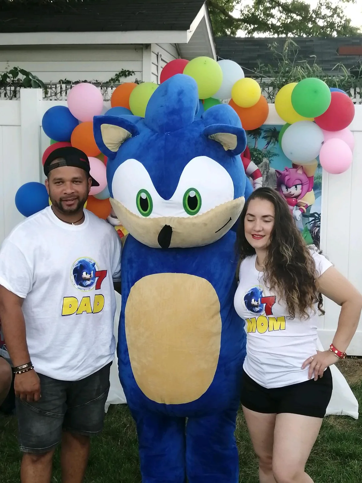 A family posing with a blue mascot in front of balloons