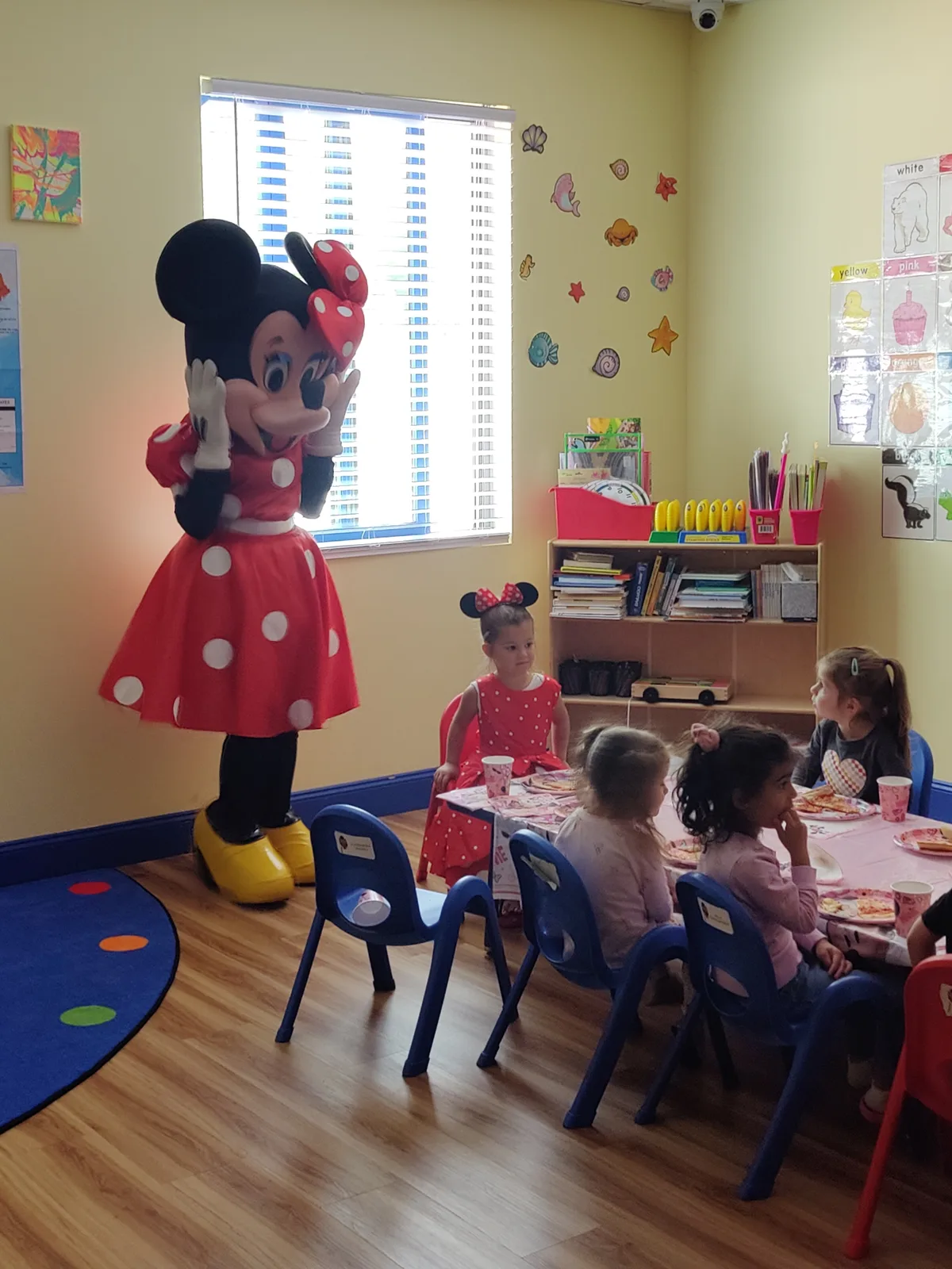 A mascot visiting children seated at a classroom party table