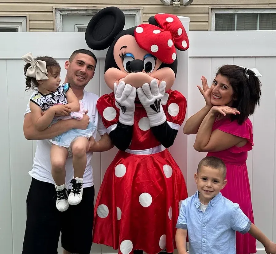A red-dressed mouse mascot posing with a family