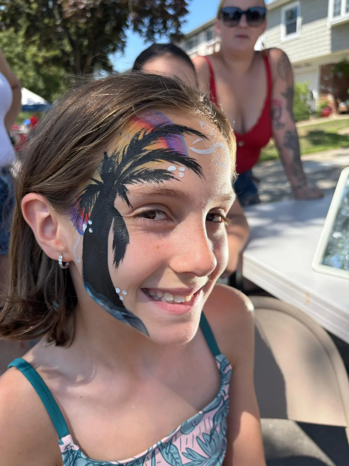 A smiling guest with a dark bird design painted around one eye