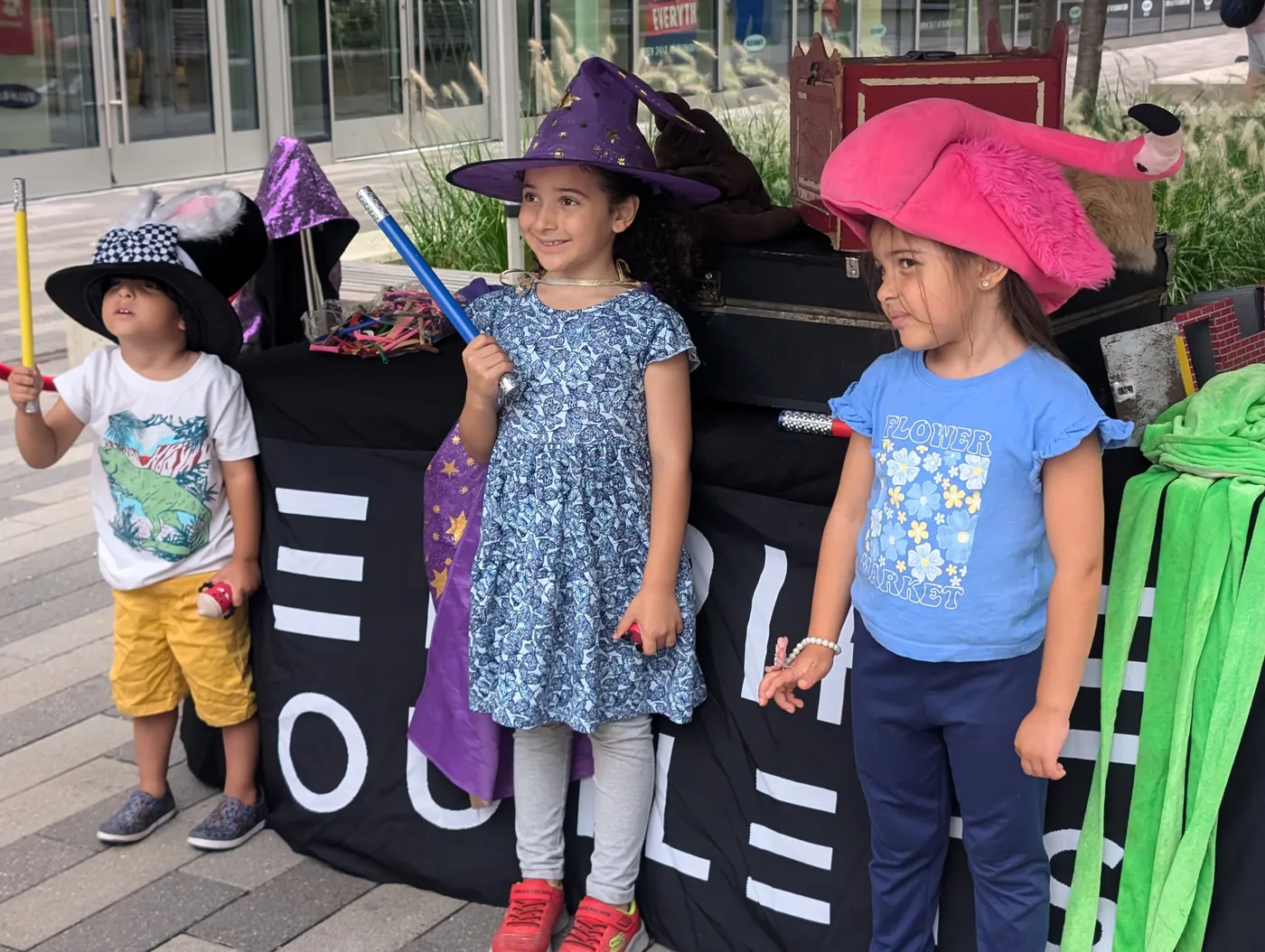 Three young volunteers wearing colorful hats beside a magic table