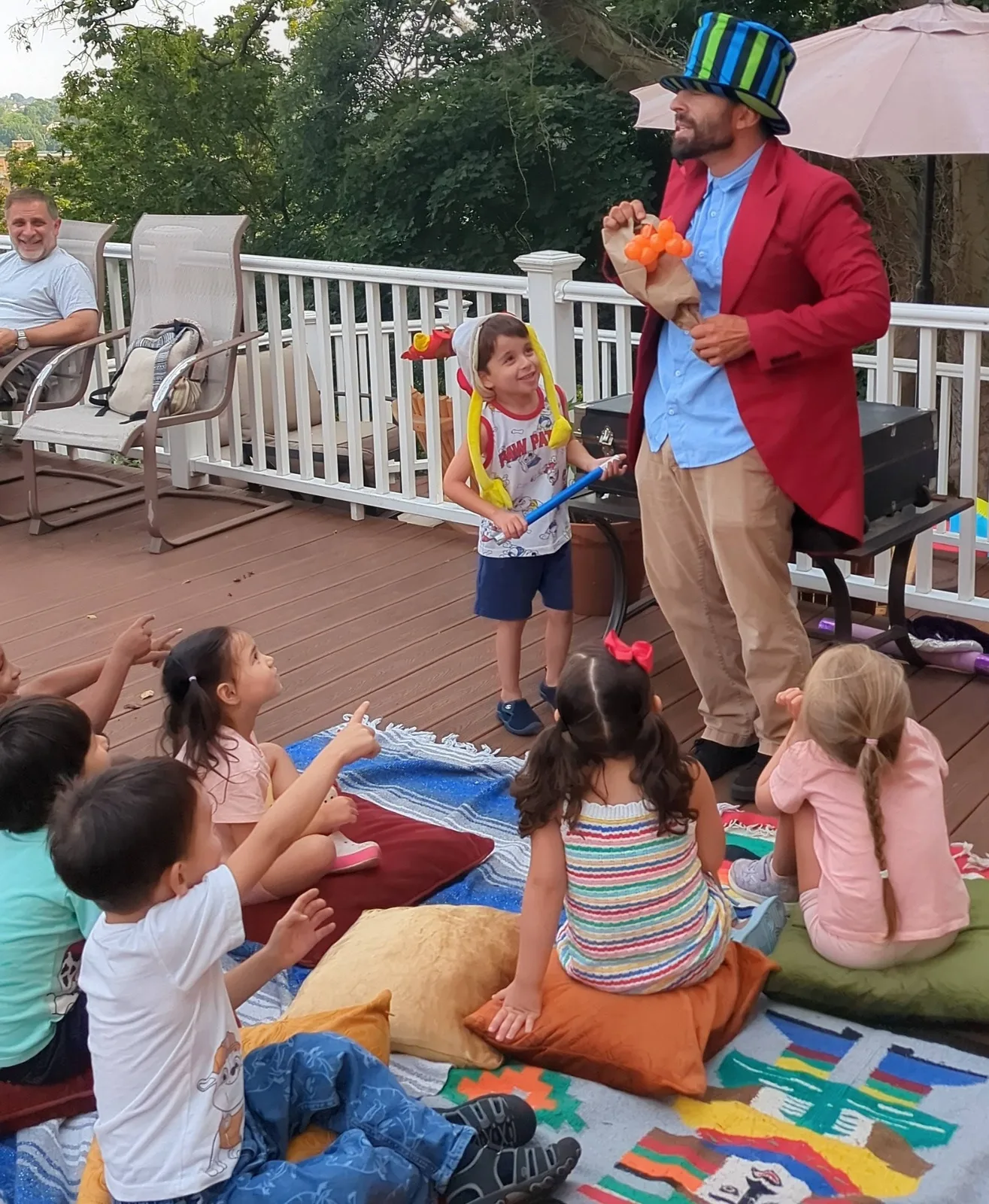 Magician in a red jacket performing for children seated outdoors