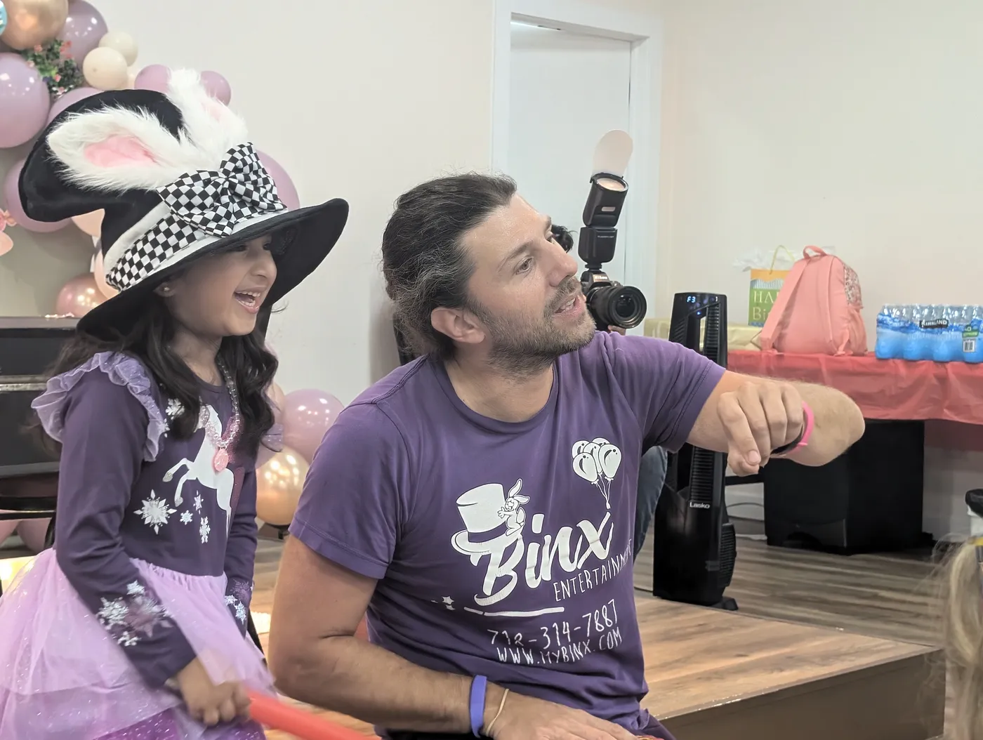 A magician in purple beside a child wearing a decorated hat