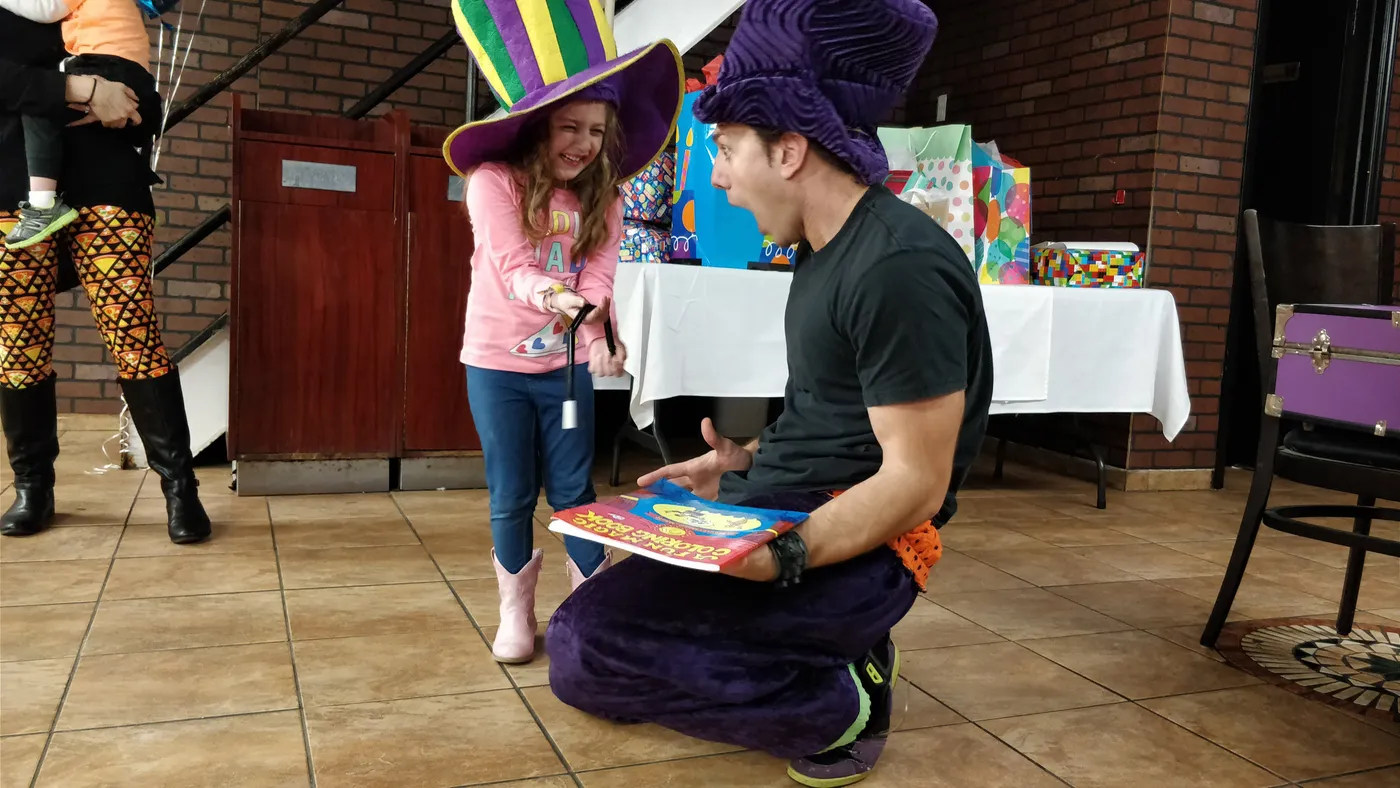 A magician performing beside a young volunteer indoors