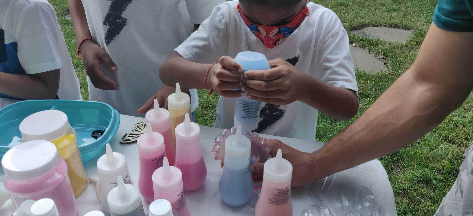 Hands filling a small bottle at an outdoor sand-art table