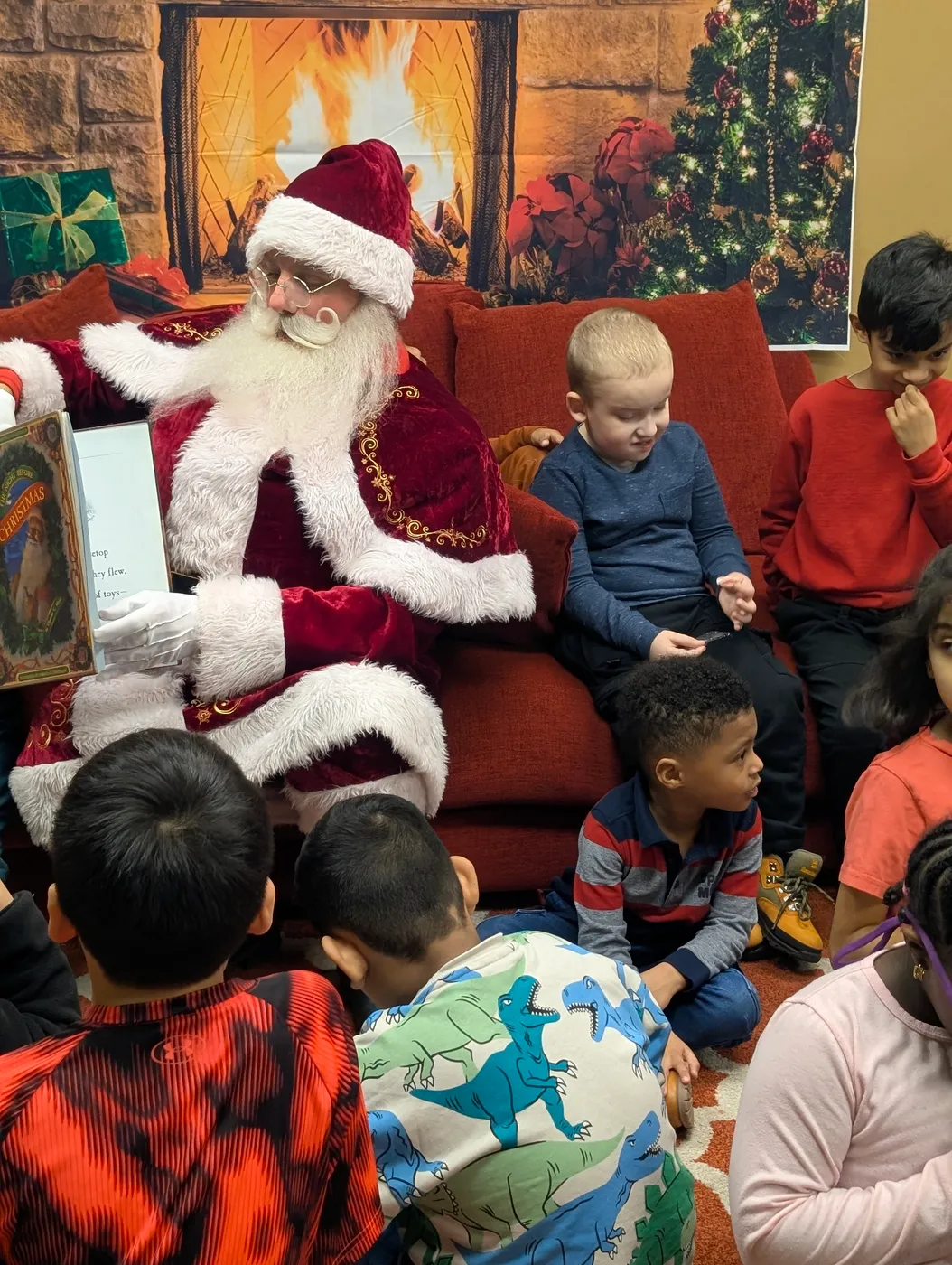 Santa sharing a story with children beside a Christmas tree
