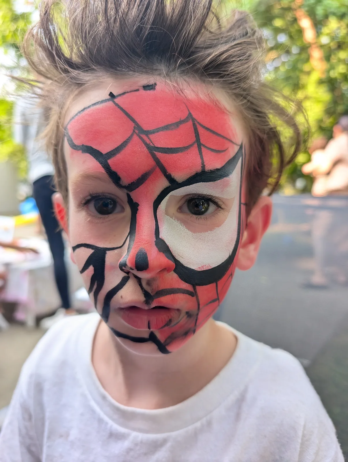A child with a red and black spider mask painted on their face