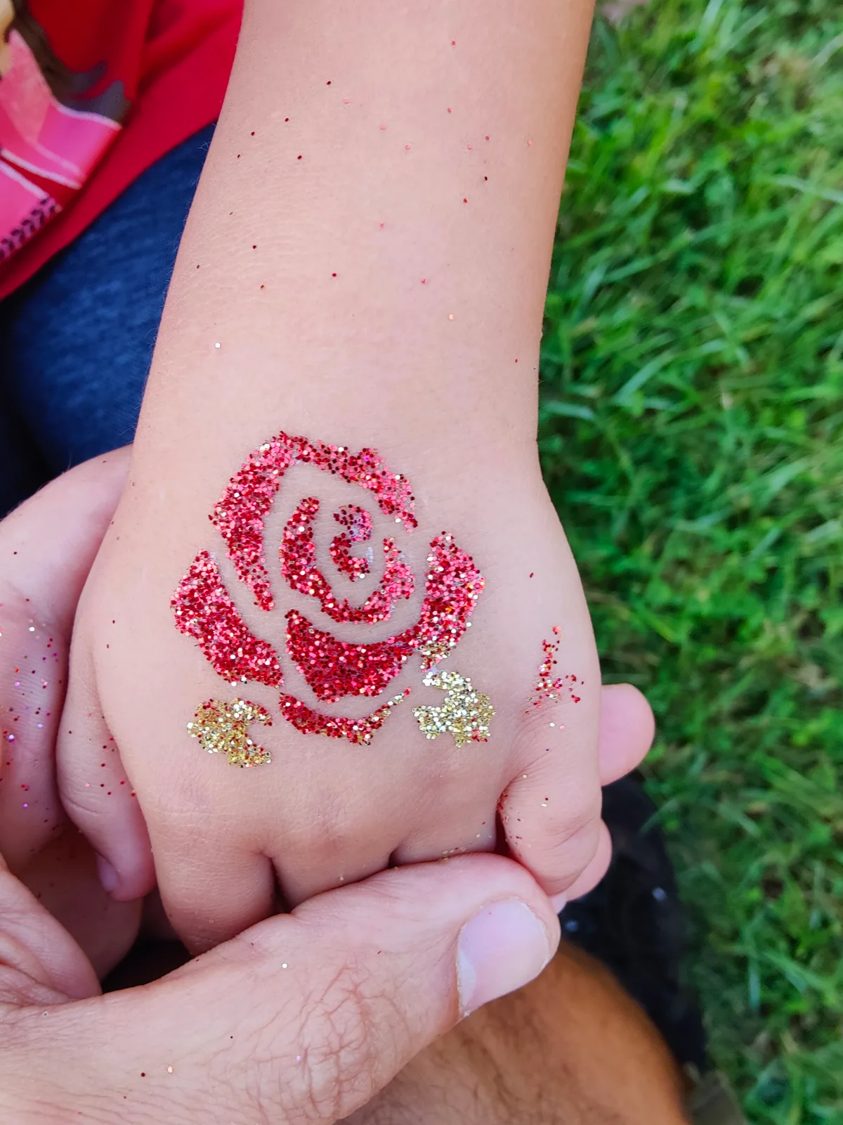Red glitter rose design on the back of a hand