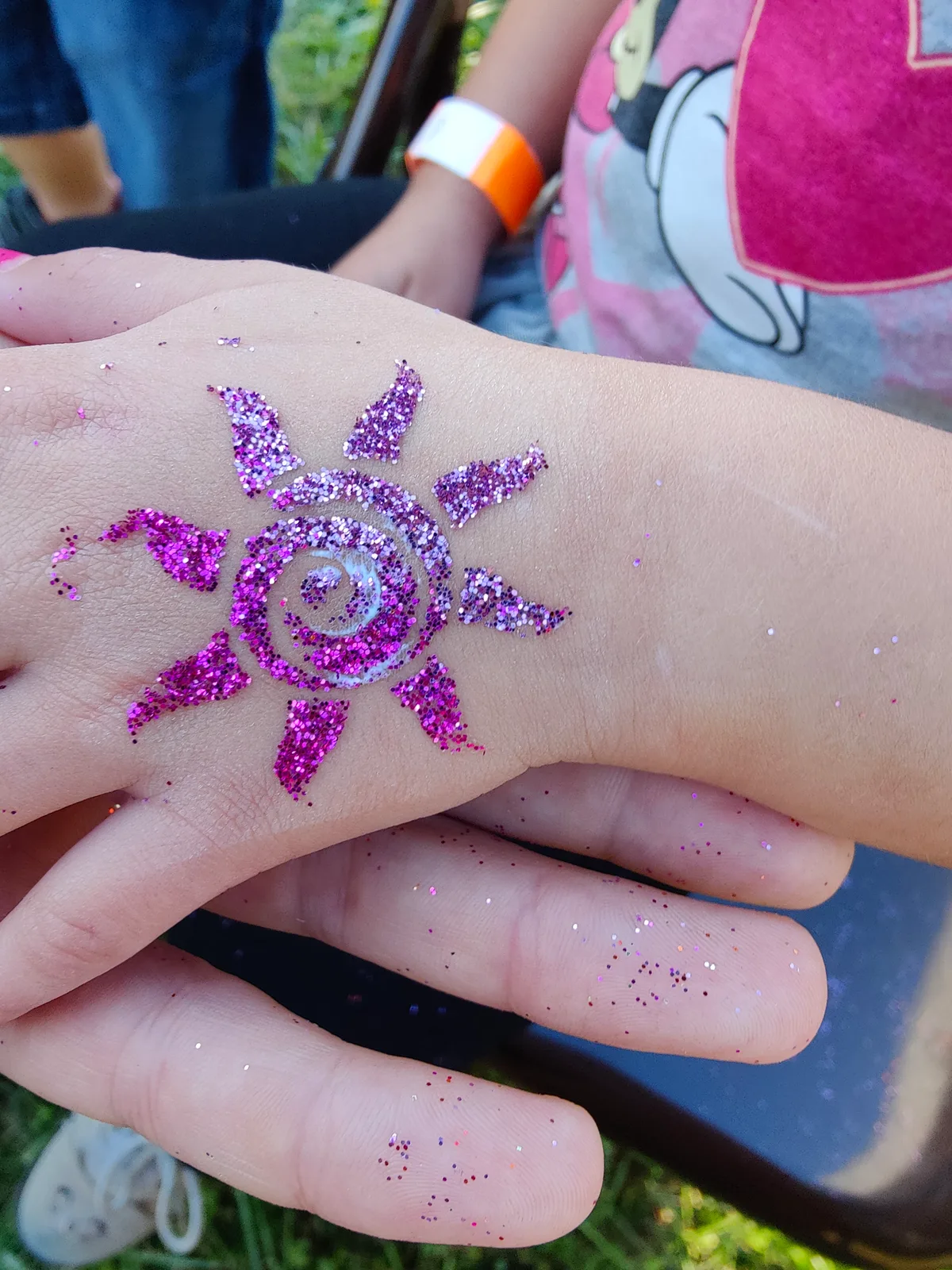 Purple glitter sun design on the back of a hand