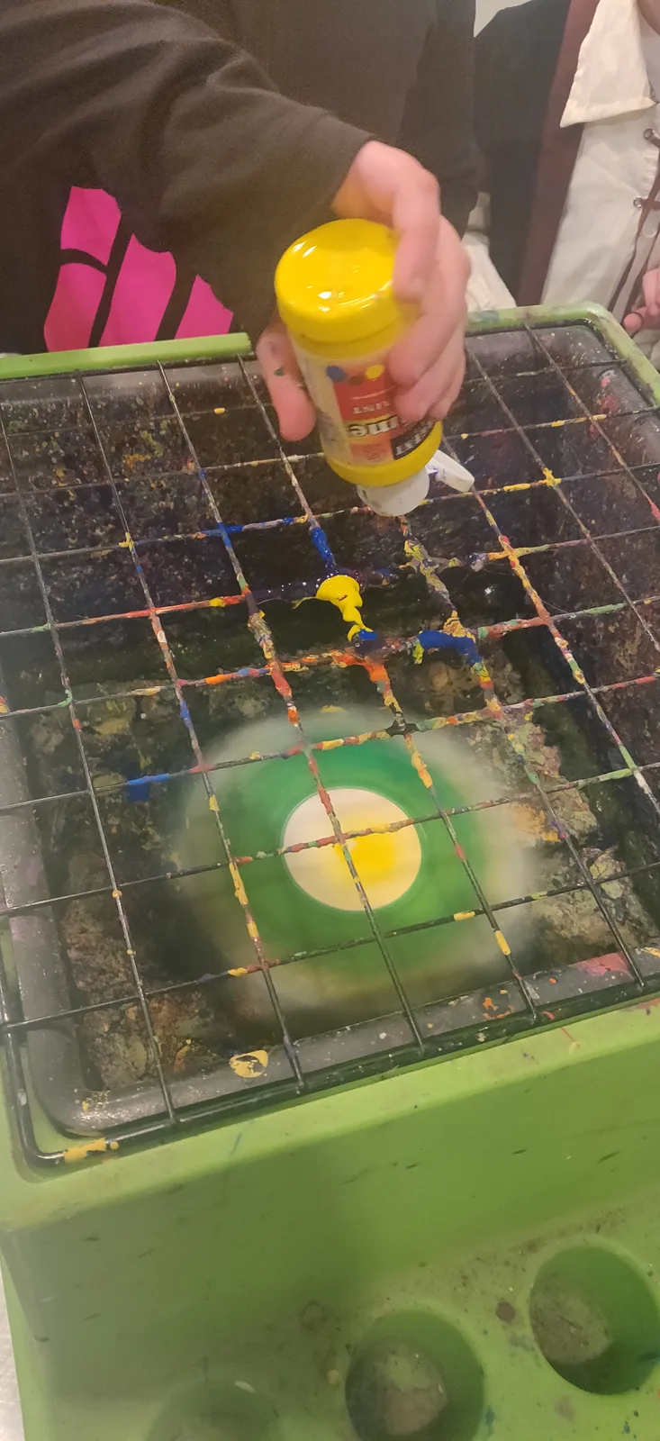 A hand squeezing yellow paint into a green spin-art machine
